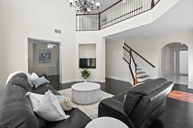 living room with ceiling fan with notable chandelier, dark hardwood / wood-style flooring, and a high ceiling