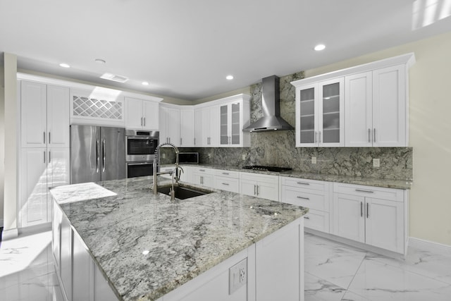 kitchen with sink, wall chimney range hood, stainless steel appliances, and a kitchen island with sink