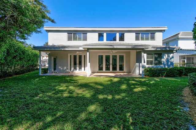 back of property with a lawn, ceiling fan, and french doors