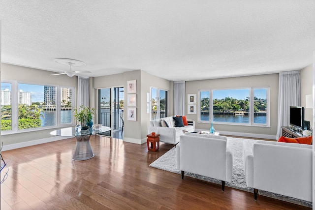 living room featuring hardwood / wood-style floors, ceiling fan, a water view, and a textured ceiling