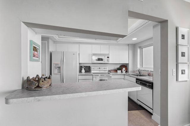 kitchen with carpet flooring, sink, kitchen peninsula, white appliances, and white cabinets