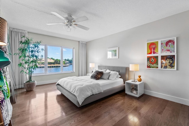 bedroom with ceiling fan, a water view, dark wood-type flooring, and a textured ceiling