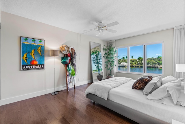 bedroom with ceiling fan, dark hardwood / wood-style flooring, a water view, and a textured ceiling