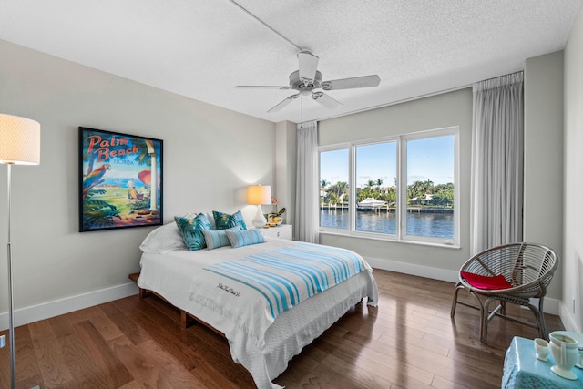 bedroom with a textured ceiling, ceiling fan, a water view, and dark wood-type flooring