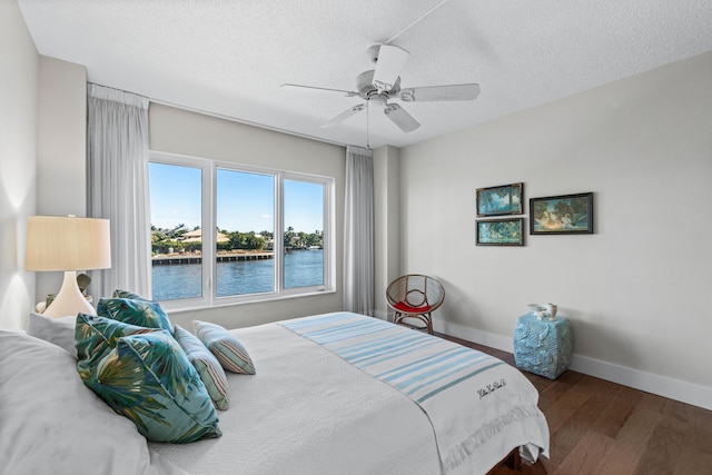 bedroom featuring ceiling fan, a water view, dark wood-type flooring, and a textured ceiling