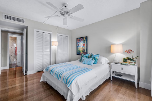 bedroom with ceiling fan, dark hardwood / wood-style flooring, a textured ceiling, and two closets