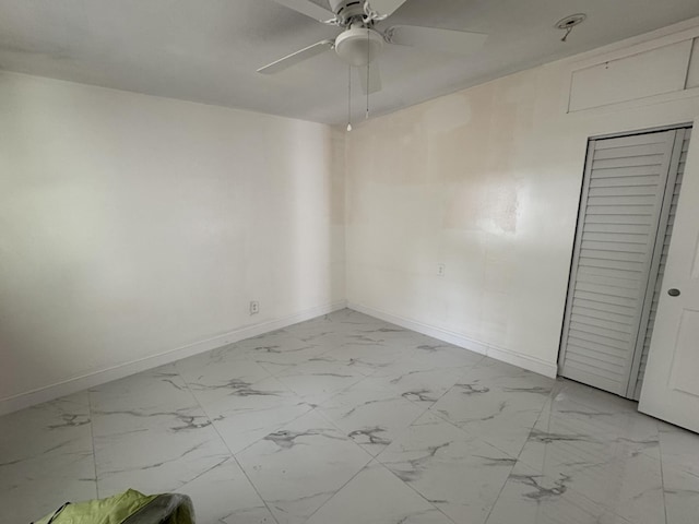 empty room featuring marble finish floor, a ceiling fan, and baseboards