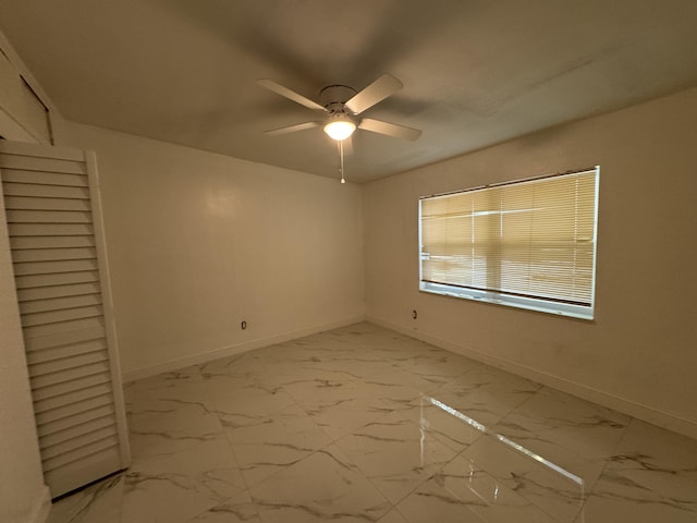 spare room with ceiling fan, marble finish floor, and baseboards