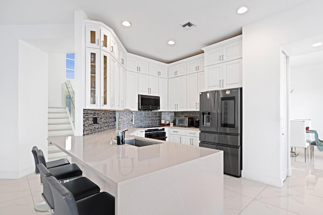 kitchen featuring a breakfast bar, appliances with stainless steel finishes, kitchen peninsula, white cabinets, and backsplash