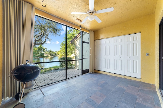 unfurnished sunroom with ceiling fan and a water view