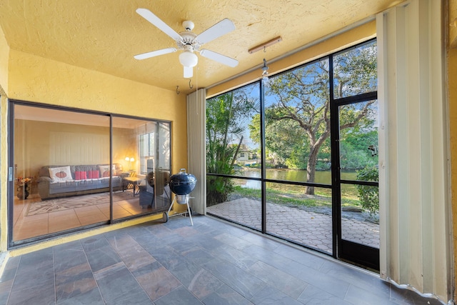 unfurnished sunroom featuring ceiling fan and a water view