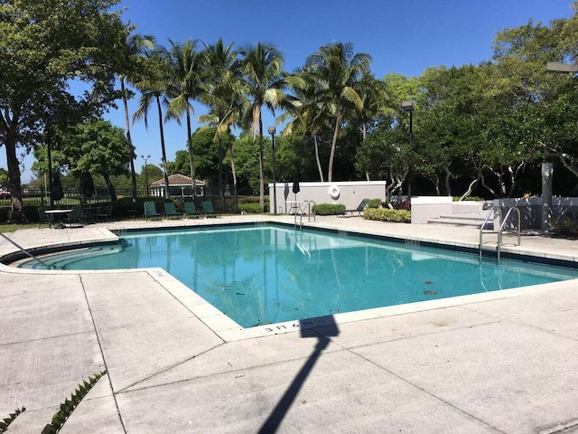 community pool featuring a patio, fence, and view of scattered trees