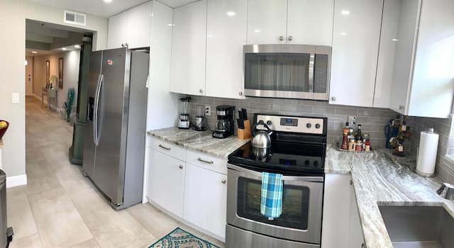 kitchen with light stone countertops, white cabinetry, stainless steel appliances, and tasteful backsplash