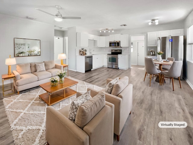 living room featuring light wood-type flooring, ceiling fan, and sink