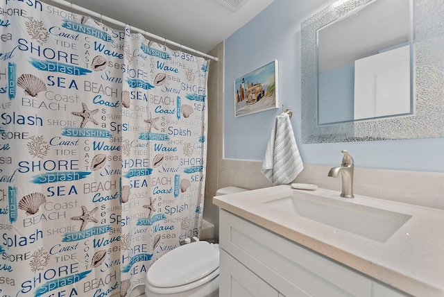 bathroom featuring vanity, toilet, and tile walls