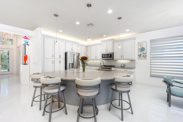 kitchen featuring appliances with stainless steel finishes, decorative light fixtures, an island with sink, sink, and light stone countertops