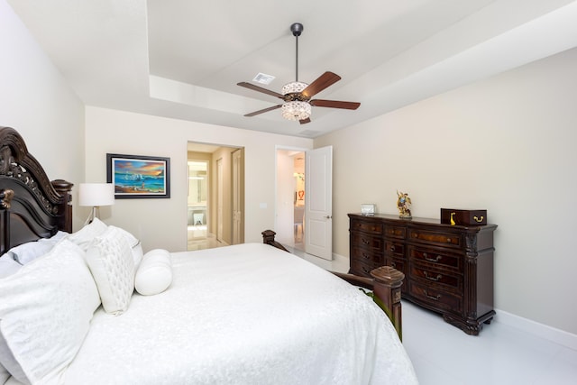 bedroom with ceiling fan, ensuite bathroom, and a tray ceiling