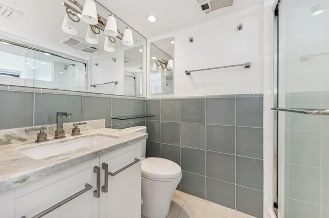 bathroom featuring tile patterned flooring, vanity, a shower with door, and tile walls