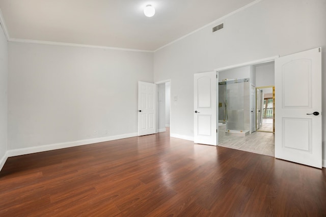 unfurnished bedroom featuring a towering ceiling, hardwood / wood-style flooring, ornamental molding, and connected bathroom