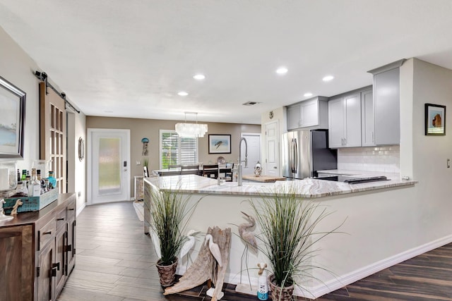 kitchen with hanging light fixtures, a barn door, light stone counters, kitchen peninsula, and stainless steel refrigerator