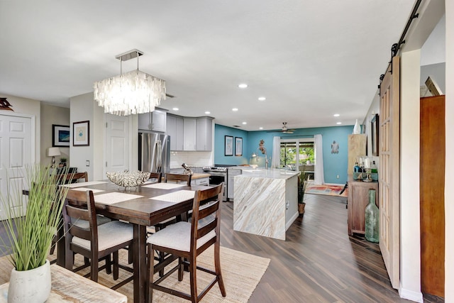 dining area with ceiling fan with notable chandelier, a barn door, dark wood-type flooring, and sink