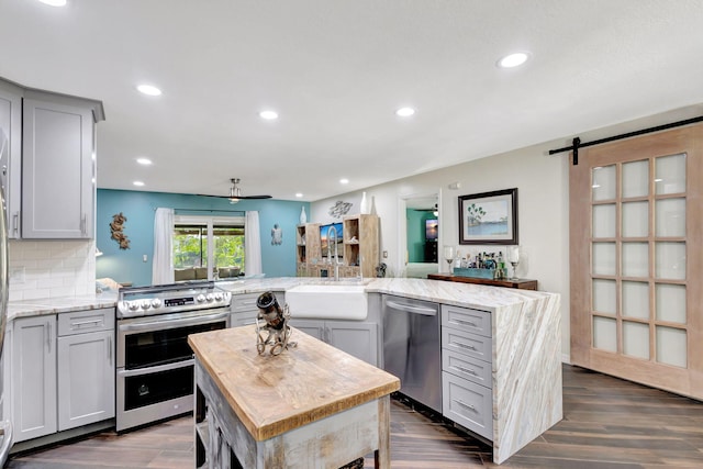 kitchen featuring gray cabinetry, stainless steel appliances, a barn door, dark hardwood / wood-style floors, and a kitchen island