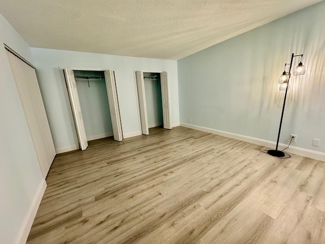 unfurnished bedroom featuring a textured ceiling, light wood-type flooring, and two closets