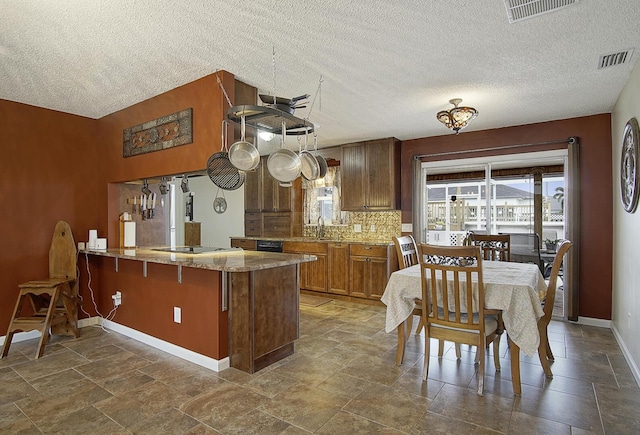 kitchen featuring backsplash, kitchen peninsula, stovetop, and a textured ceiling