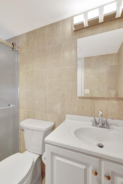 bathroom featuring an enclosed shower, vanity, toilet, and tile walls