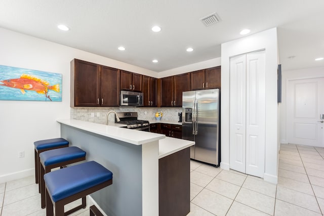 kitchen with tasteful backsplash, kitchen peninsula, a kitchen bar, light tile patterned floors, and appliances with stainless steel finishes