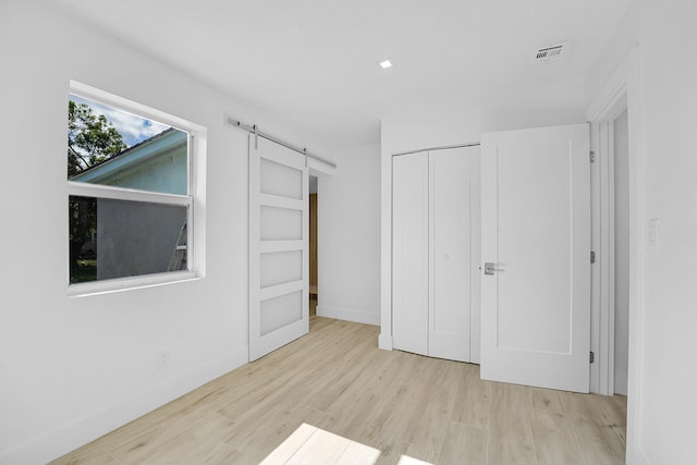 unfurnished bedroom with a barn door, a closet, and light hardwood / wood-style floors