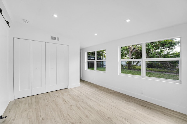 unfurnished bedroom featuring a barn door, light hardwood / wood-style flooring, and a closet