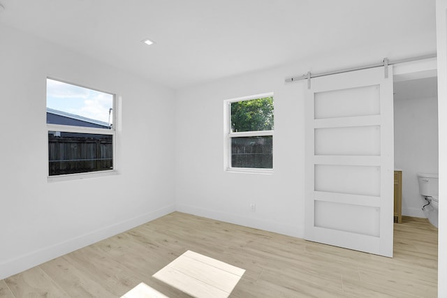 unfurnished bedroom with a barn door, light hardwood / wood-style flooring, and multiple windows