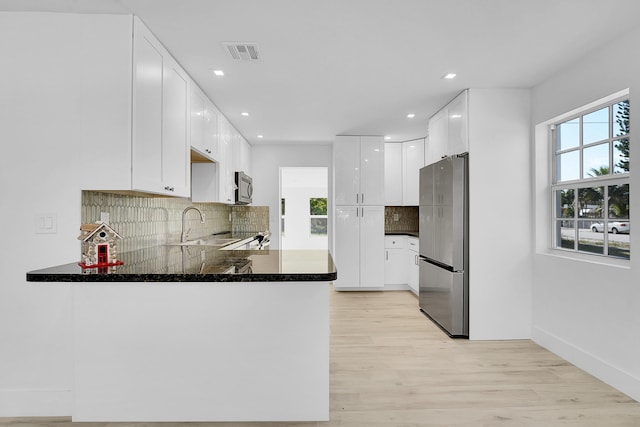 kitchen with white cabinets, light wood-type flooring, appliances with stainless steel finishes, tasteful backsplash, and kitchen peninsula