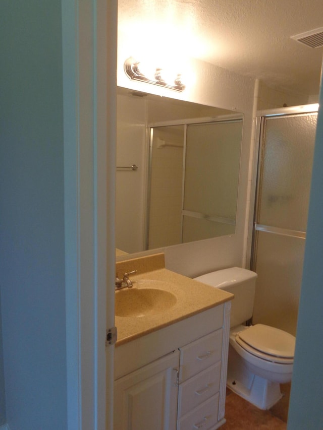 bathroom with a shower with door, vanity, a textured ceiling, and toilet