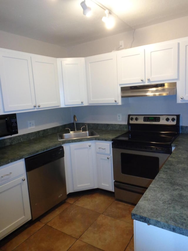 kitchen with appliances with stainless steel finishes, white cabinetry, dark tile patterned flooring, and sink