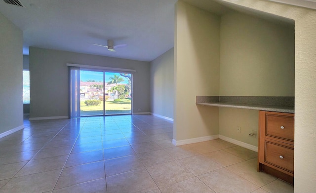 tiled empty room with ceiling fan and built in desk