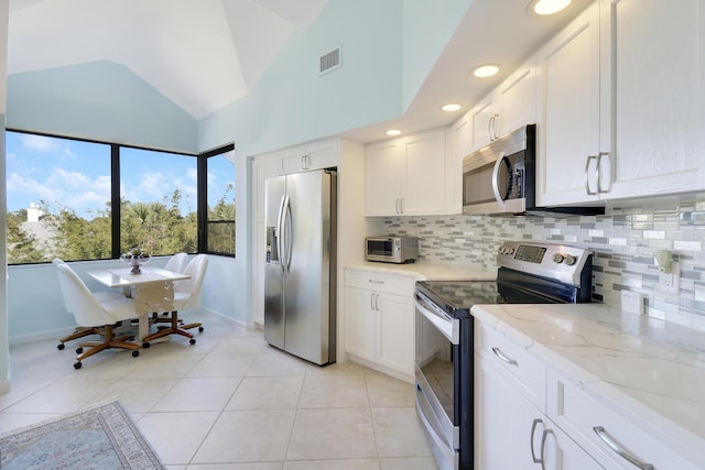 kitchen featuring backsplash, stainless steel appliances, light tile patterned floors, white cabinetry, and lofted ceiling