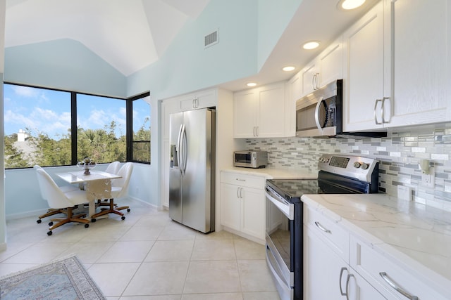 545 Bay Colony Dr N, Juno Beach, FL 33408 - kitchen with appliances with stainless steel finishes, decorative backsplash, white cabinets, vaulted ceiling, and light tile patterned floors