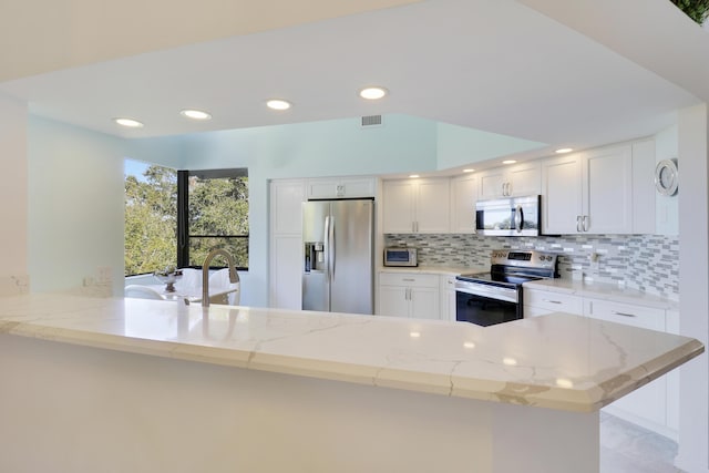 kitchen with light stone countertops, backsplash, kitchen peninsula, white cabinets, and appliances with stainless steel finishes