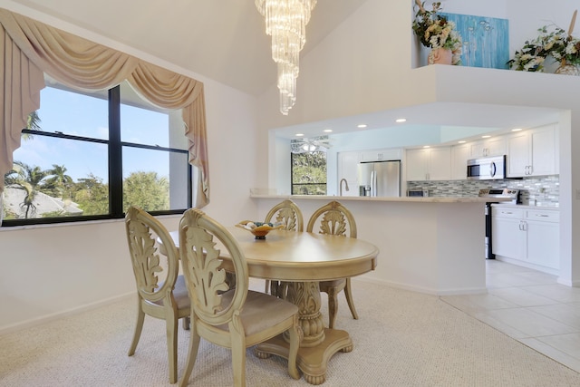 tiled dining space featuring ceiling fan with notable chandelier, high vaulted ceiling, a wealth of natural light, and sink