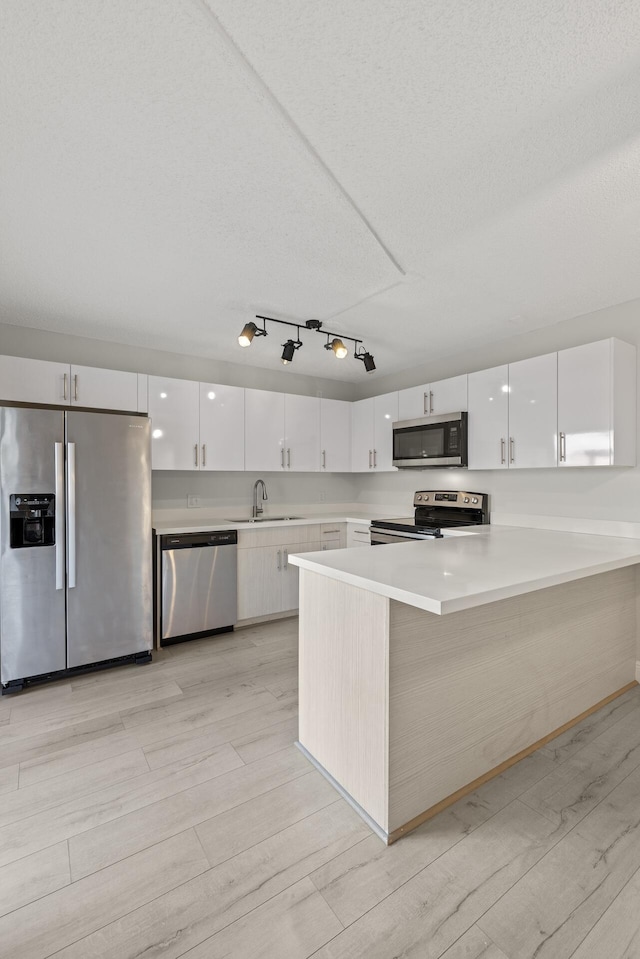 kitchen featuring kitchen peninsula, white cabinets, stainless steel appliances, and light wood-type flooring