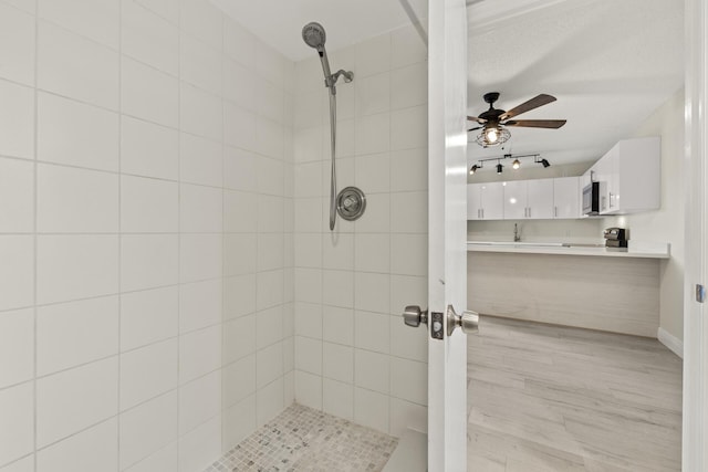 bathroom featuring ceiling fan, wood-type flooring, and tiled shower