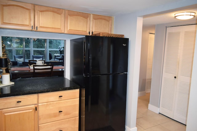 kitchen with light brown cabinetry, light tile patterned floors, and black fridge