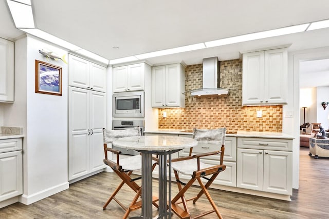 kitchen with appliances with stainless steel finishes, backsplash, wall chimney range hood, dark hardwood / wood-style floors, and white cabinetry