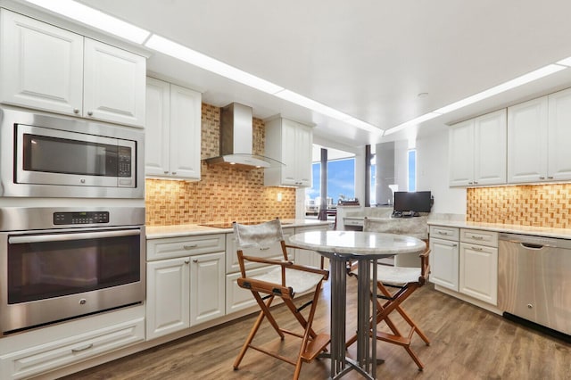 kitchen featuring white cabinets, wall chimney range hood, and appliances with stainless steel finishes