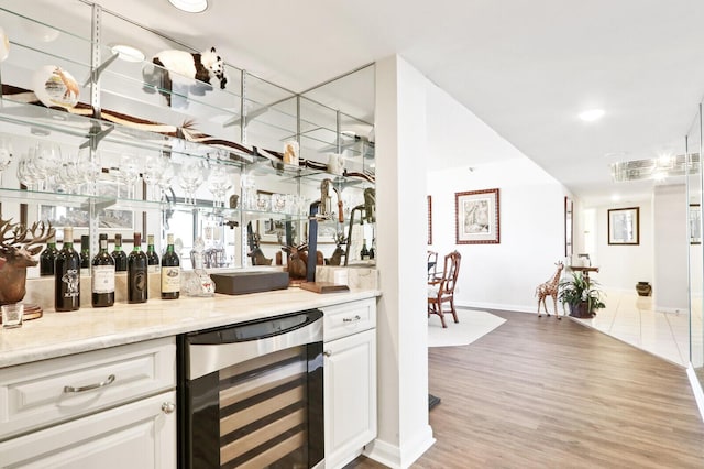 bar featuring white cabinetry, light hardwood / wood-style flooring, beverage cooler, and light stone counters