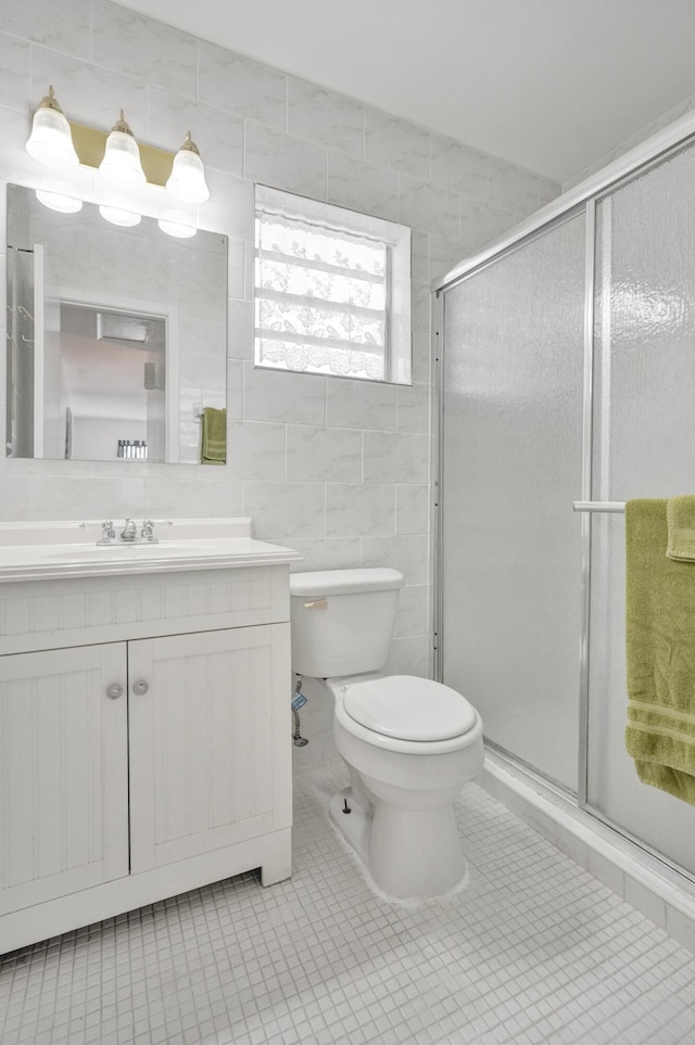 bathroom with tile patterned floors, vanity, a shower with shower door, and tile walls