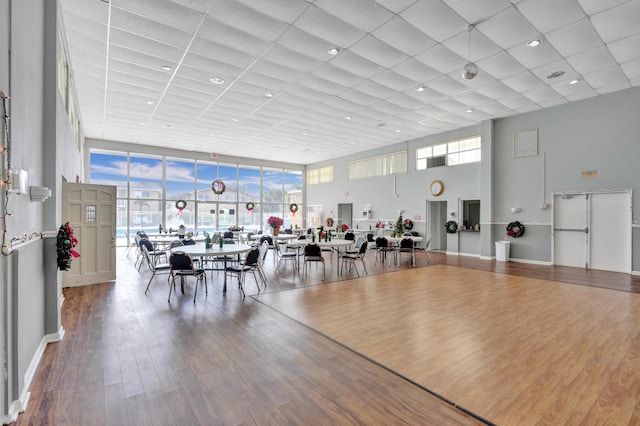 dining space featuring wood-type flooring, a towering ceiling, and a drop ceiling