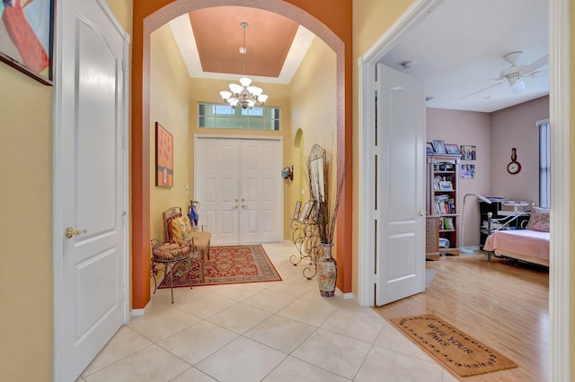 entryway with ceiling fan with notable chandelier, light wood-type flooring, and a tray ceiling